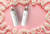 Haetsia Primavera Argan Oil Shampoo and Conditioner bottles on a soft pink background surrounded by ivory sculpted ornaments